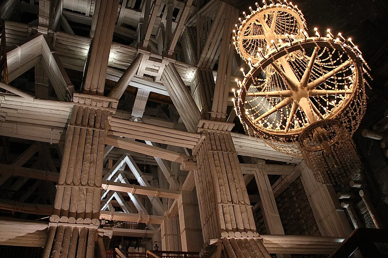 A vast chamber braced by timber frames, with a wooden chandelier overhead